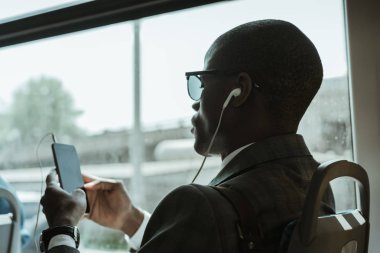 Şık emin iş adamı tren çekerken smartphone kullanarak kulaklık
