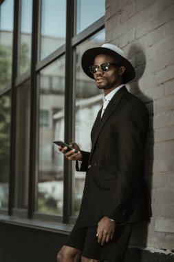 Fedora şapka ve şehirde smartphone kullanarak moda Afrikalı-Amerikalı adam