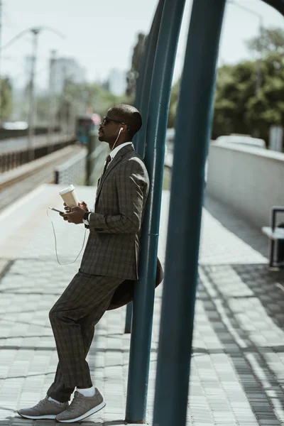 Elegante Empresário Confiante Ouvindo Música Segurando Xícara Café Estação Ferroviária — Fotografia de Stock