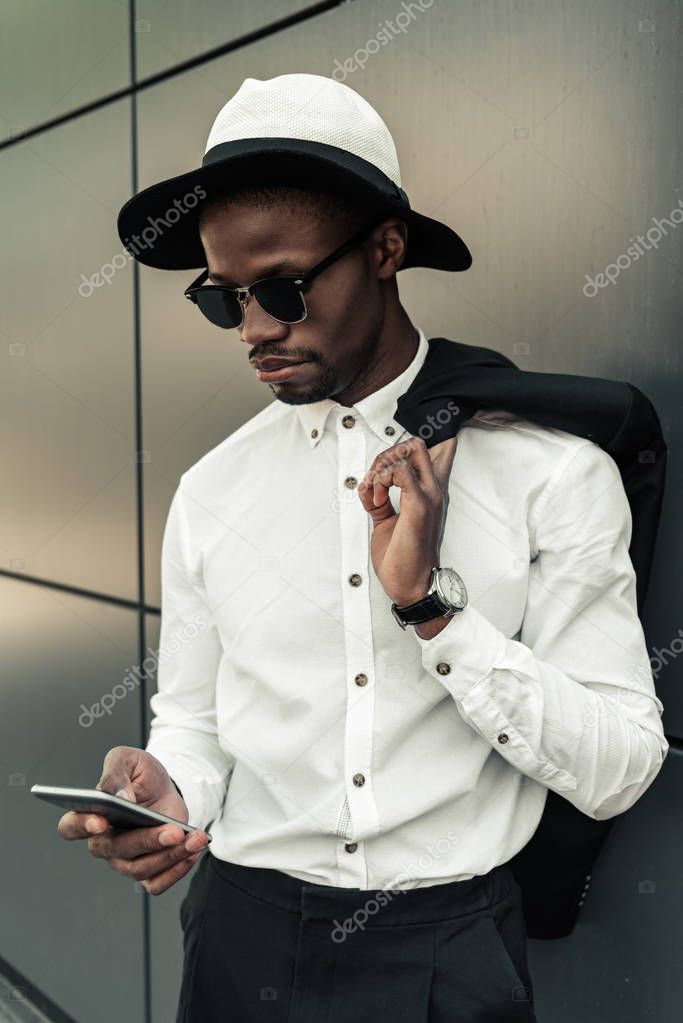 Fashionable african american businessman wearing fedora hat and using smartphone