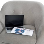 Laptop with blank screen and business newspaper on grey armchair