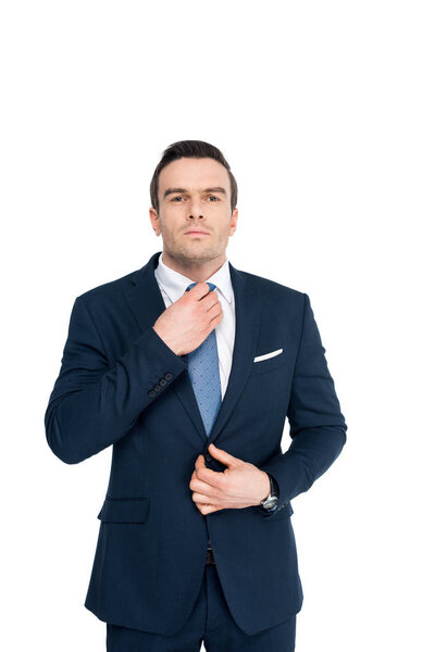 handsome middle aged businessman adjusting necktie and looking at camera isolated on white