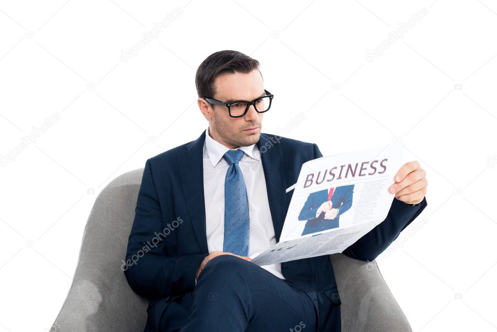 serious businessman in eyeglasses reading newspaper while sitting in armchair isolated on white 