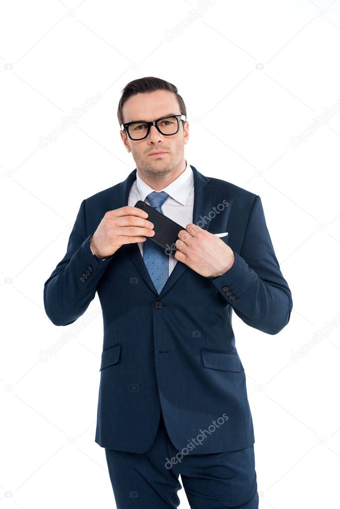 handsome businessman in eyeglasses looking at camera while holding smartphone isolated on white