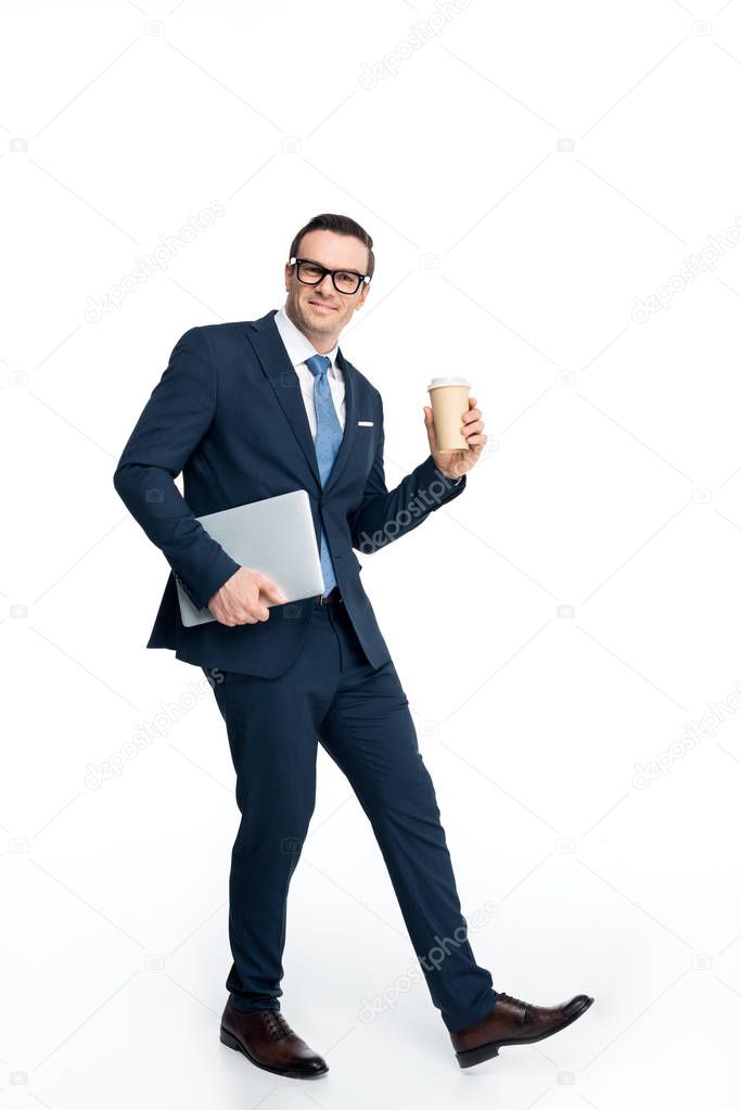 full length view of handsome businessman holding laptop and paper cup and smiling at camera isolated on white 