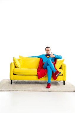 handsome male superhero sitting on couch and showing thumb up on white clipart