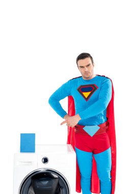 handsome superhero pointing with finger at washing machine and soap powder isolated on white clipart