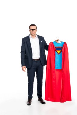 businessman in eyeglasses holding hanger with superhero costume and looking at camera isolated on white  clipart