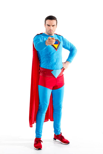 полный обзор уверенного мужчины-супергероя, стоящего с рукой на талии и указывающего на камеру, изолированную на белом
 