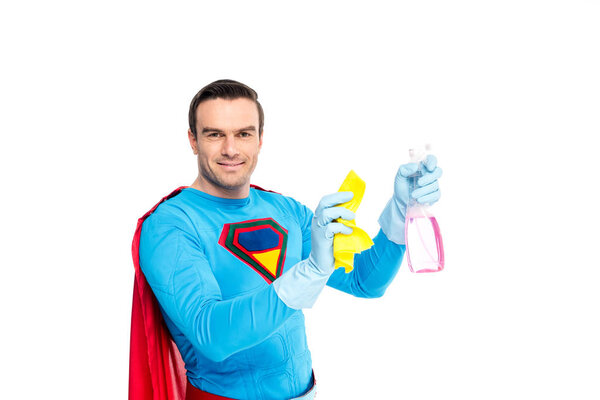 handsome smiling superman holding rag and spray bottle with detergent isolated on white