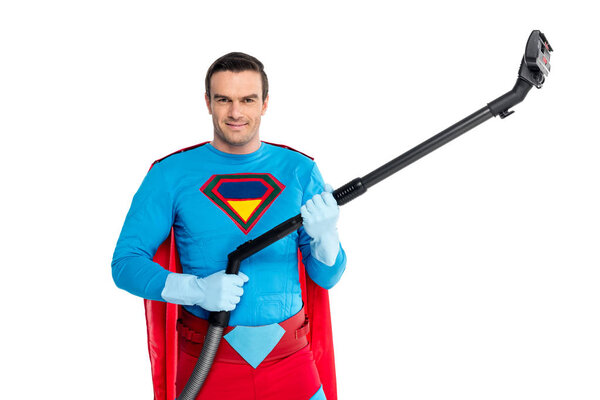 handsome man in superhero costume holding vacuum cleaner and smiling at camera isolated on white