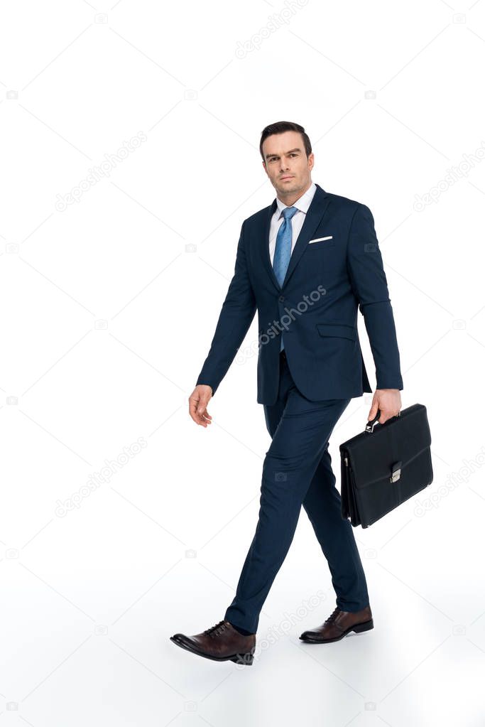 full length view of businessman with briefcase walking and looking at camera on white