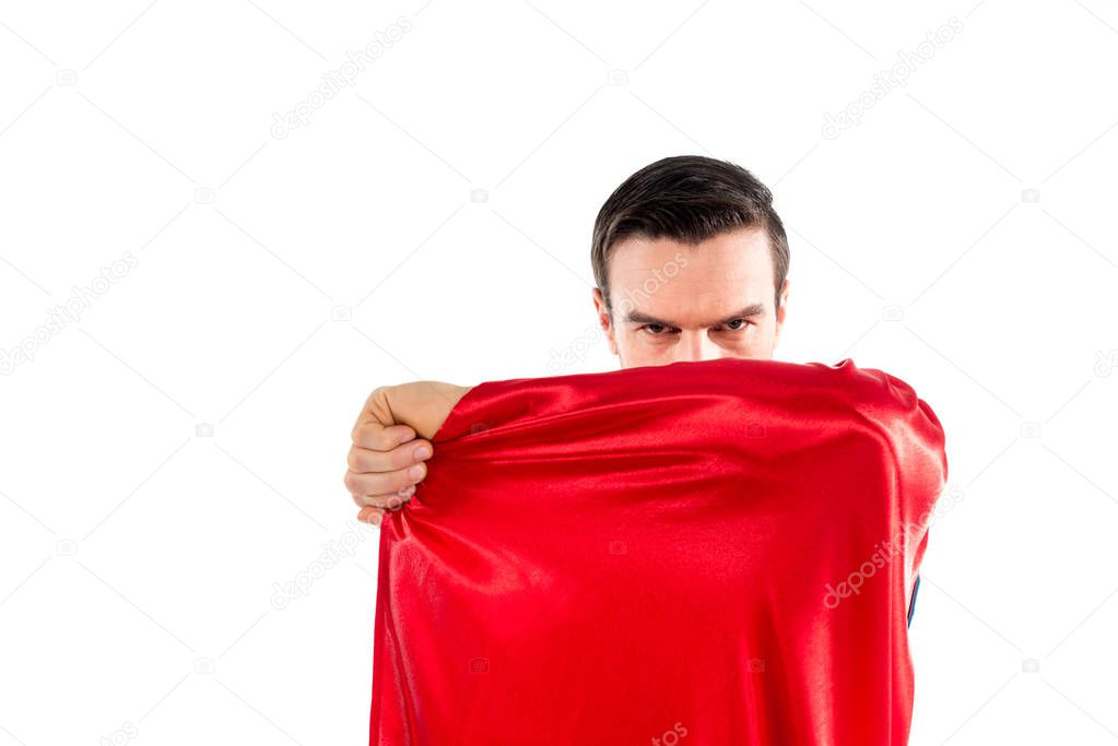 handsome male superhero hiding behind cloak and looking at camera isolated on white
