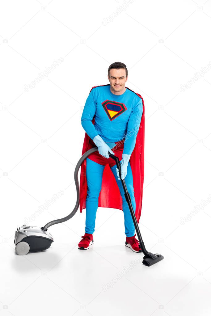 superman in rubber gloves using vacuum cleaner and smiling at camera on white