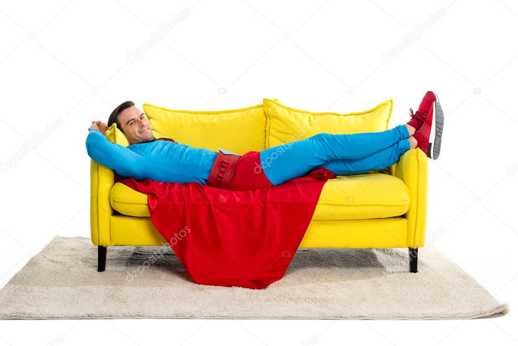 superman lying on couch and smiling at camera isolated on white