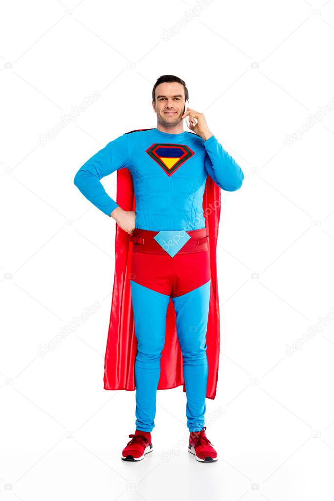 full length view of handsome male superhero talking by smartphone and smiling at camera isolated on white