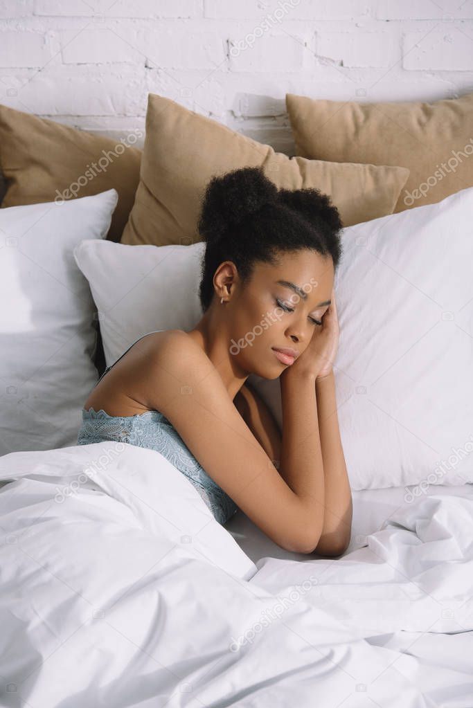 attractive african american girl sleeping on pillows in bed