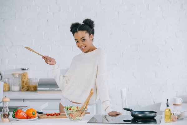 happy young woman preparing breakfast at kitchen and looking at camera