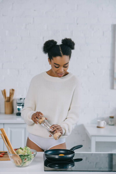 beautiful young woman peppering scrambled egg on frying pan at kitchen