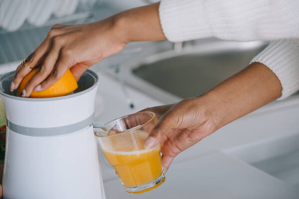 cropped shot of woman squeezing fresh orange juice at kitchen