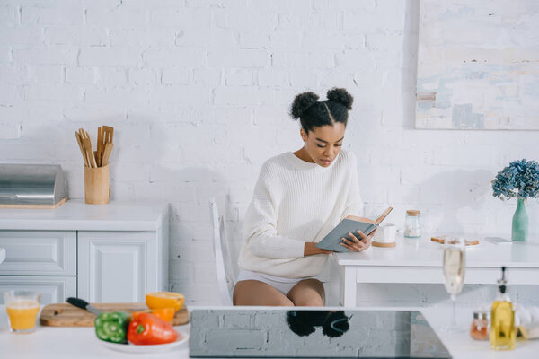 beautiful young woman reading book at kitchen in morning