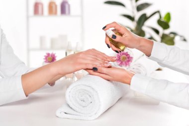 çiçek ve güzellik salonu havlu ile masada kadının ellerinde aroma yağı püskürtme manikürcü kısmi görünümünü 