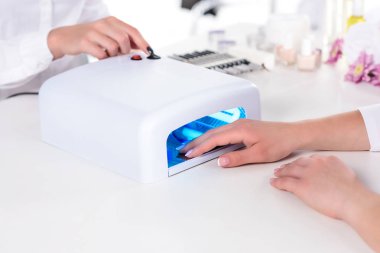 uv lamba güzellik salonu masada düğmeye manikürcü sırasında elini tutarak kadının kırpılmış görüntü