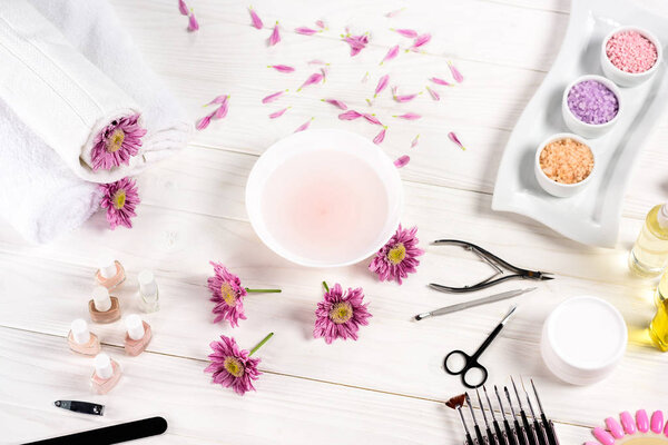 elevated view of bath for nails at table with flowers, petals, towels, nail polishes, nail file, cuticle pusher, nail clippers, scissors, sea salt, cream container, aroma oil bottles and nail samples of nail varnishes at table 