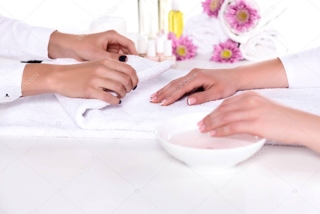 cropped image of manicurist rolling towel to dry hand of woman while she having bath for nails in beauty salon