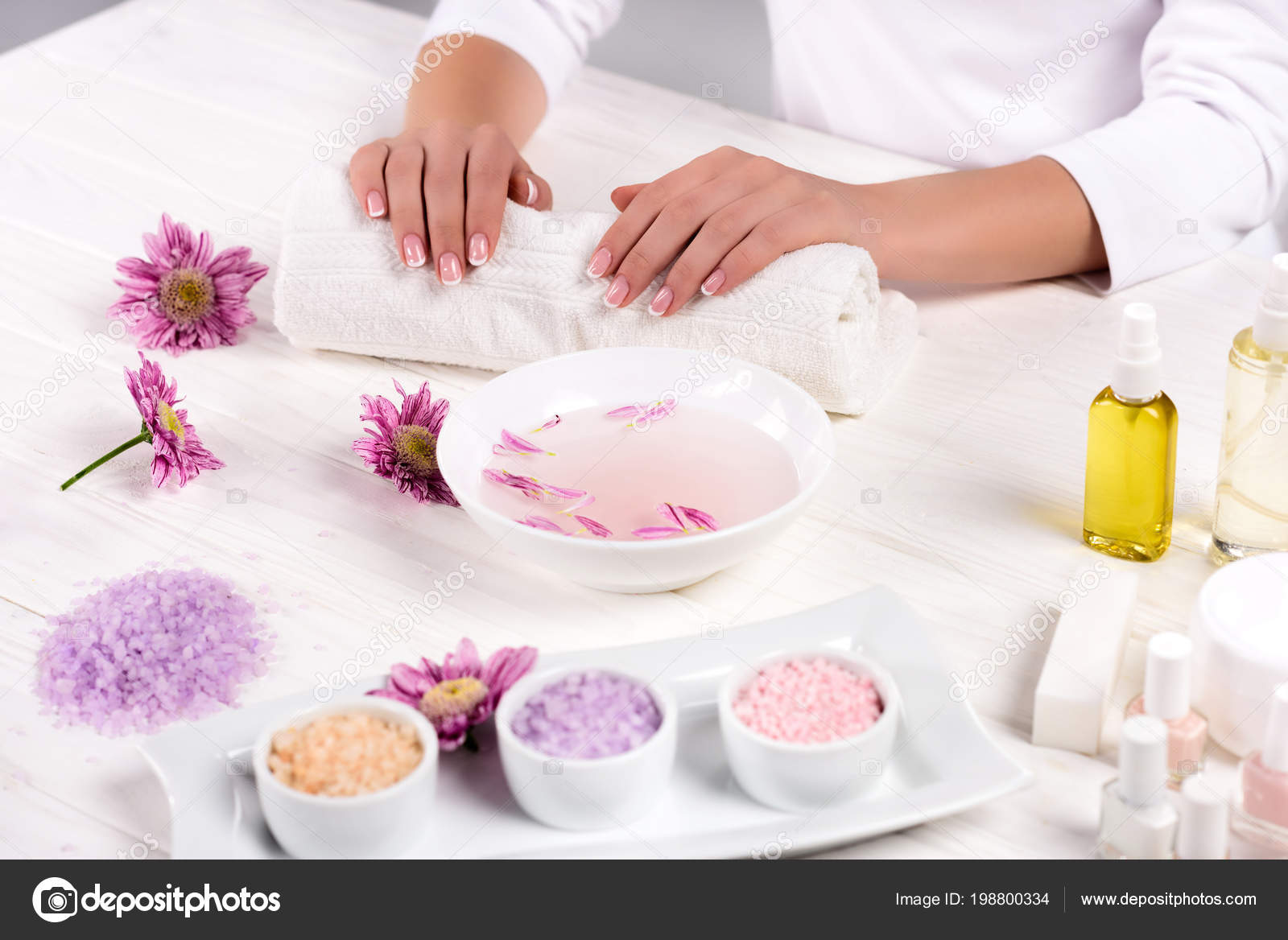 Imagem recortada de mãos dadas na toalha para procedimento de manicure, mesa com flores, sal do mar colorido, recipiente de creme, frascos de óleo de aroma