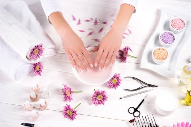 kadının güzellik salonunda banyo masasında görmek çiçek, havlu, renkli deniz tuzu, aroma yağ şişeleri, tırnak cilaları, Krem Konteyner ve manikür çivi için alma kırpılmış görüntü 