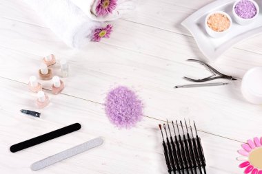 elevated view of colorful sea salt, towels, flowers, nail polishes, cream container, nail clippers, cuticle pusher, nail files and samples of nail varnishes for manicure at table in beauty salon  clipart
