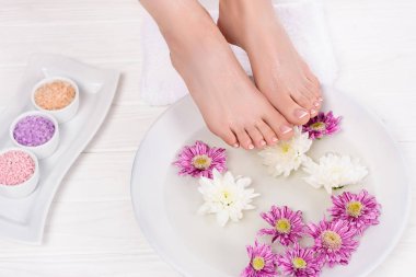 cropped shot of barefoot woman receiving bath for nails with sea salt and flowers in beauty salon clipart