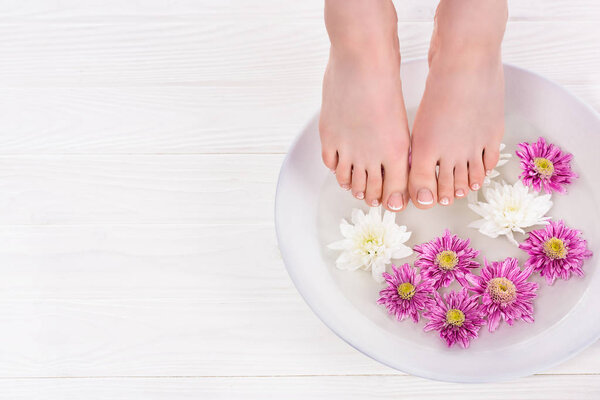 частичный вид босиком женщины, принимающей ванну для ногтей цветы в салоне красоты
