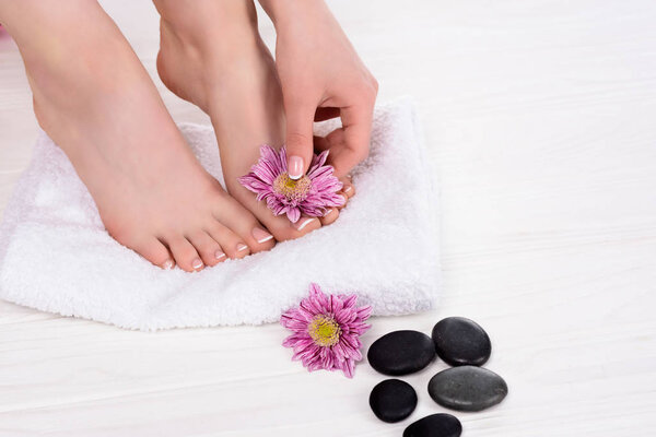partial view of barefoot woman on spa treatment with towel, flowers and spa stones 