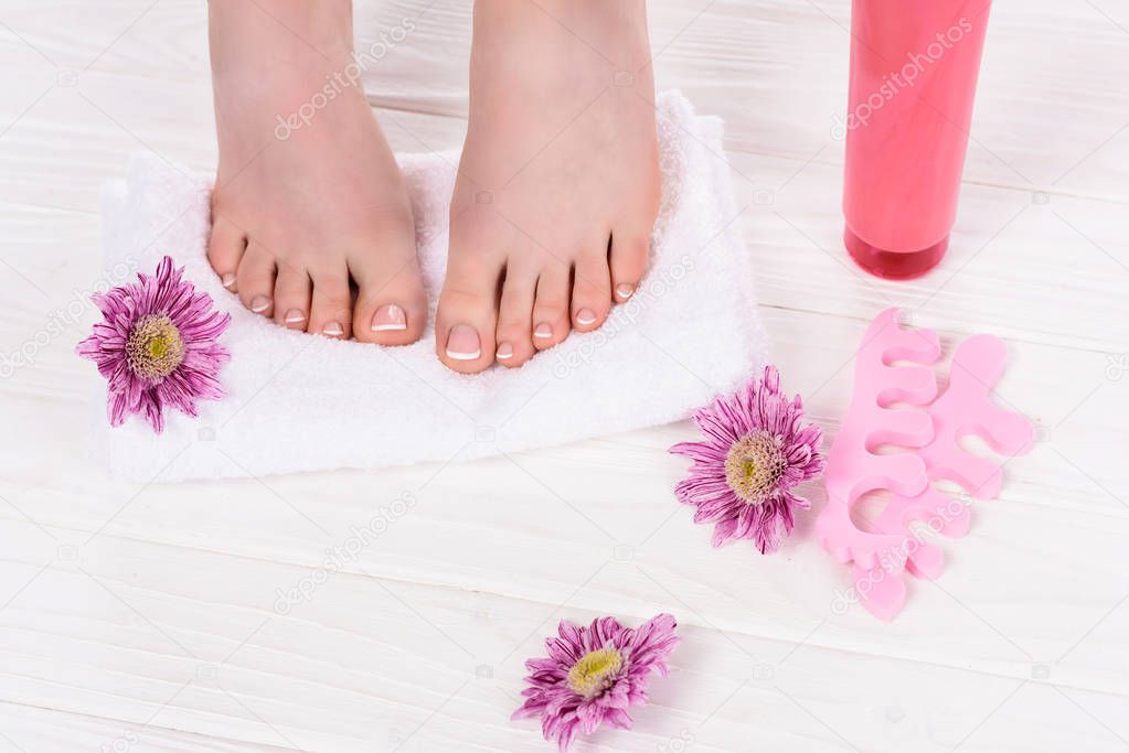cropped image of barefoot woman on towel near flowers, toe finger separators and cream container in beauty salon 
