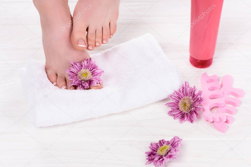 cropped image of barefoot woman on towel near flowers, toe finger separators and cream container in beauty salon 