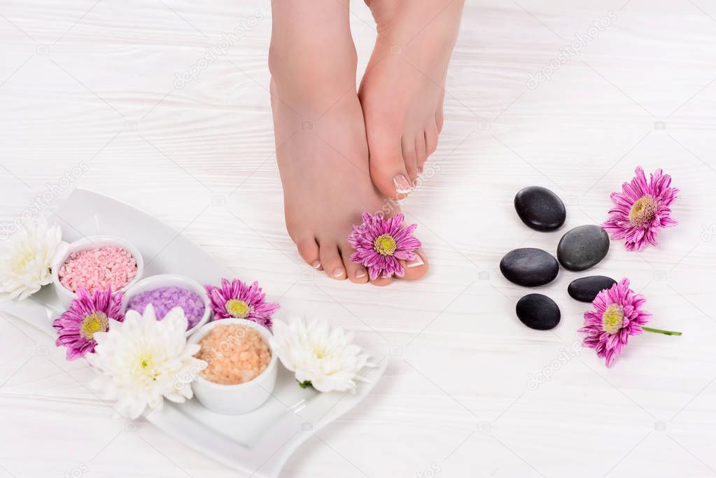 cropped image of barefoot woman on spa treatment with flowers, colorful sea salt and spa stones 