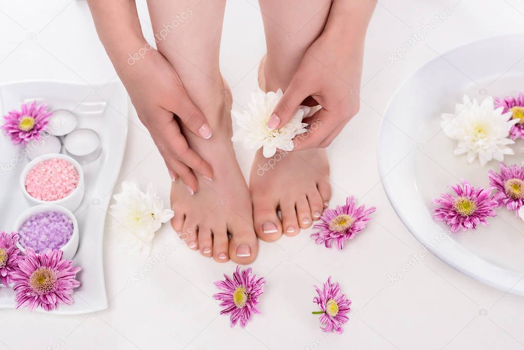 cropped shot of barefoot woman with flowers, candles, colorful sea salt and bath for nails in beauty salon 