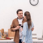 Beautiful adult couple clinking glasses of wine at kitchen