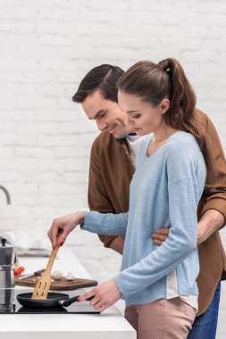 happy husband embracing his wife from behind while she cooking