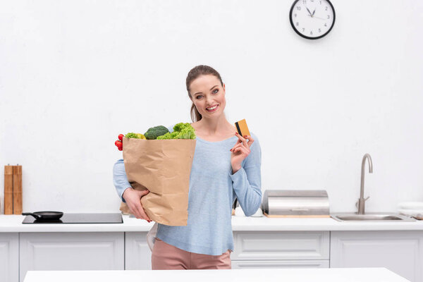 happy adult woman with paper bag and credit card at kitchen