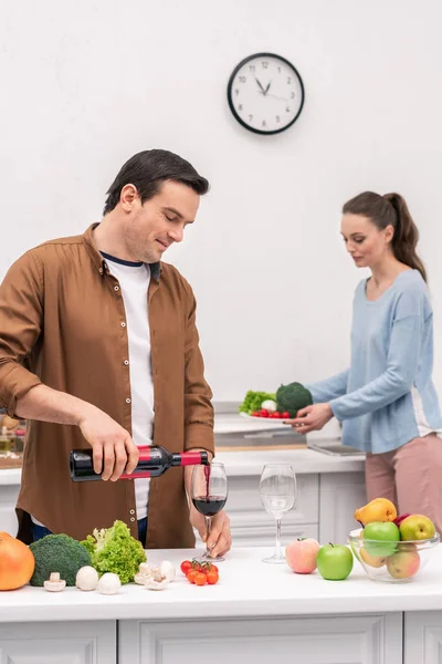 Glücklicher Ehemann Schenkt Frau Während Der Zubereitung Des Abendessens Wein — kostenloses Stockfoto