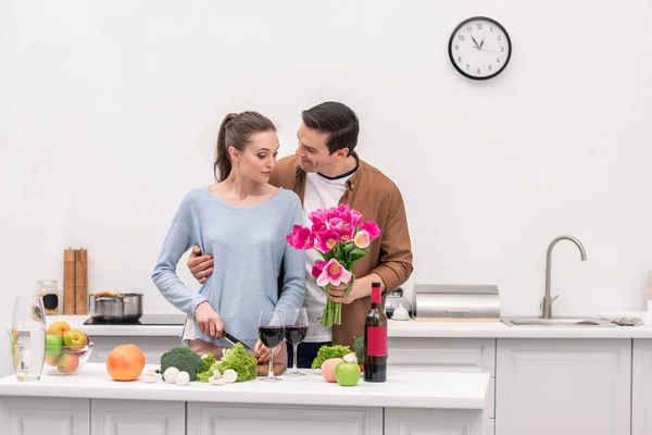 Happy Adult Man Presenting Tulips Bouquet Wife While She Cooking — Free Stock Photo