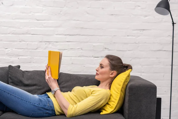 Samping Melihat Wanita Dewasa Membaca Buku Sambil Berbaring Sofa Rumah — Stok Foto