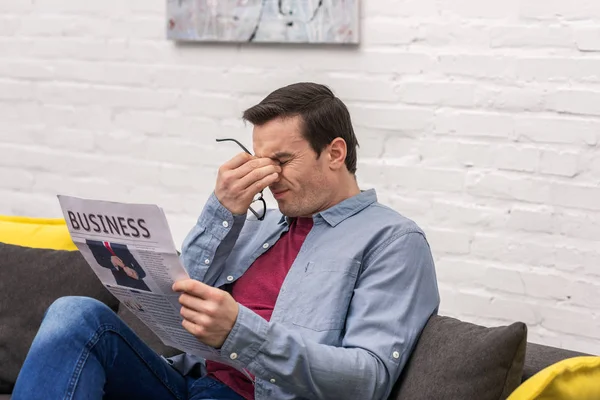 tired adult man rubbing eyes while reading newspaper