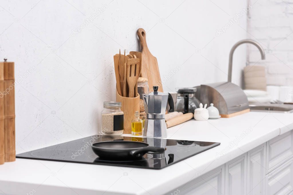 frying pan on induction panel at modern kitchen with various utensils