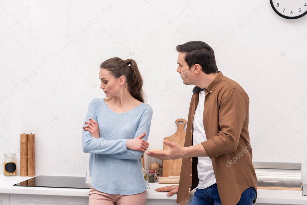 mad adult man looking at wife while she ignoring him after argument at kitchen