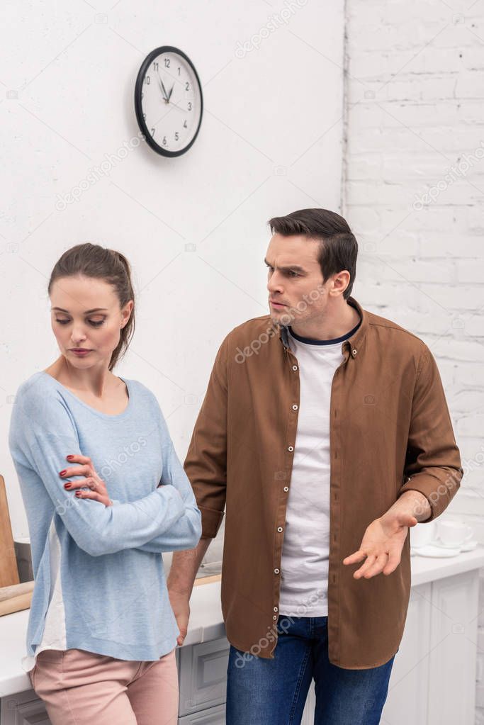 angry adult man looking at wife while she ignoring him after quarrel at kitchen