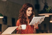 portrét ženy s šálkem kávy, čtení novin u stolu s notebookem v kavárně